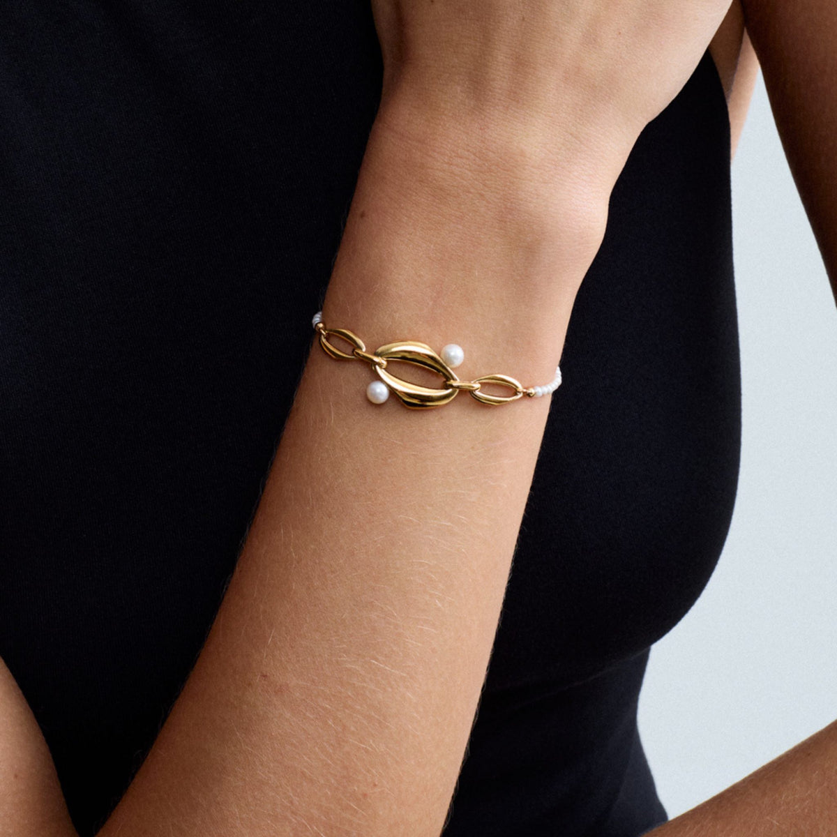 Detailed close-up of a model wearing the Audrey Swan Bracelet in 18K gold-plated sterling silver featuring white freshwater cultured pearls.